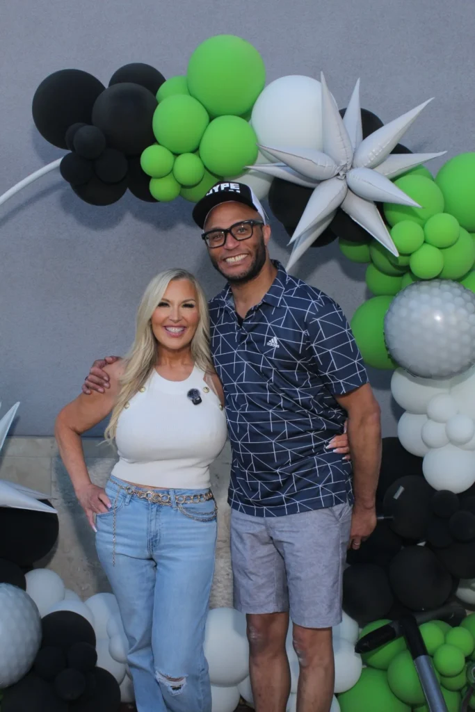 Couple posing in front of a green, black and white balloon arch at a photo booth
