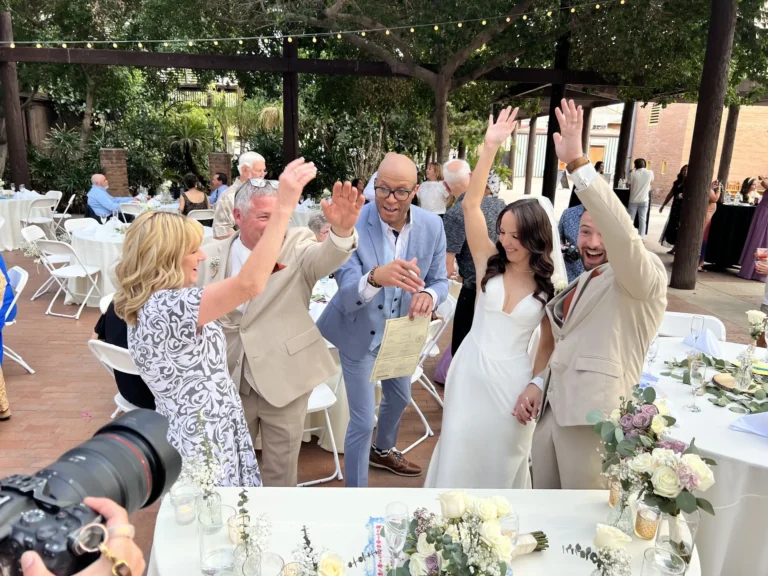 Newlyweds raising the signed marriage license as seated guests cheer at an outdoor reception
