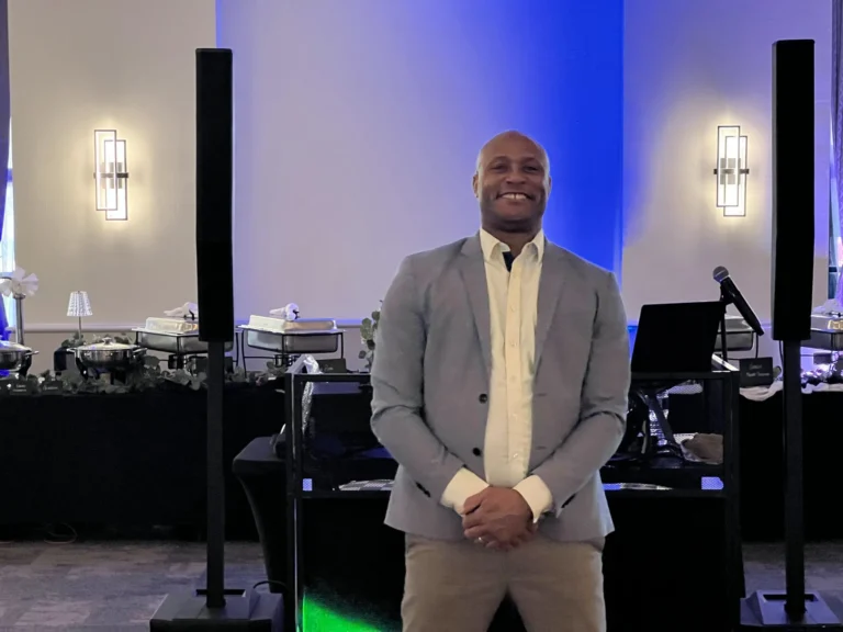 Hype Man Entertainment DJ standing beside his booth in a ballroom washed in blue uplighting