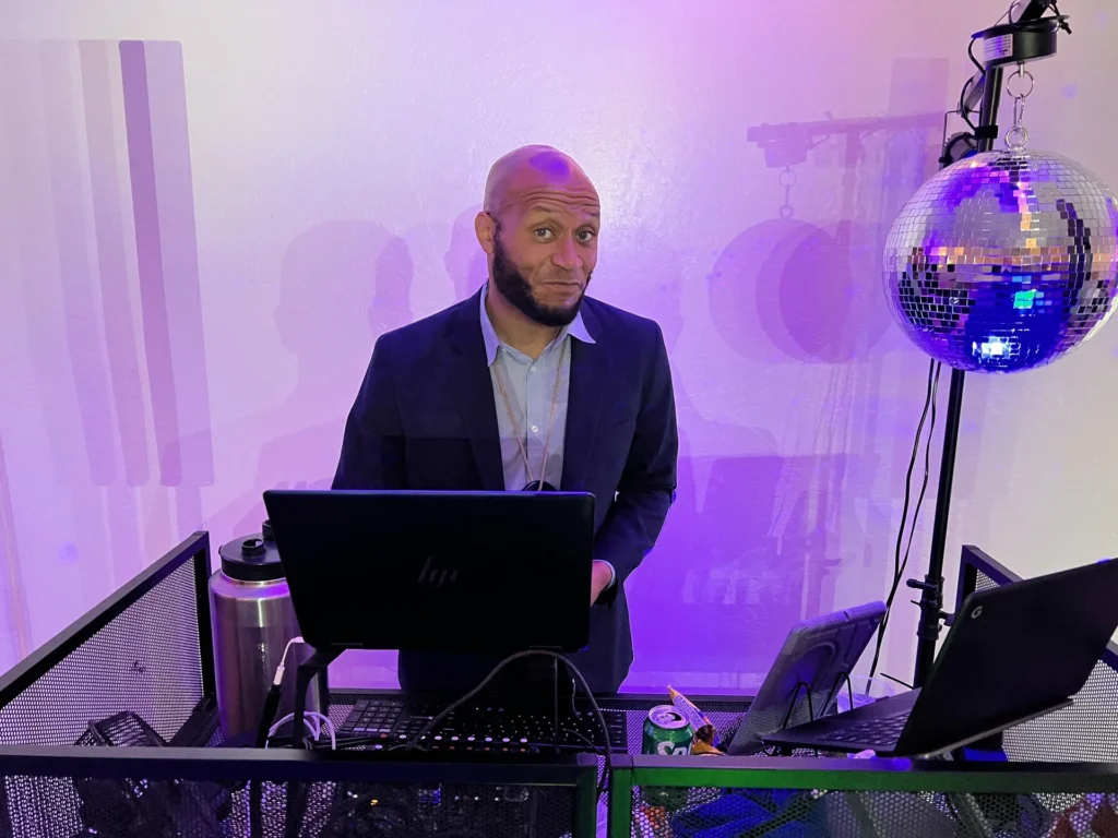 DJ booth set up with a mirrored disco ball and purple uplighting at an indoor venue