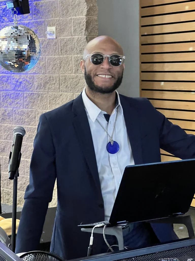 Hype Man Entertainment DJ on the microphone at his booth beside a disco ball and brick wall
