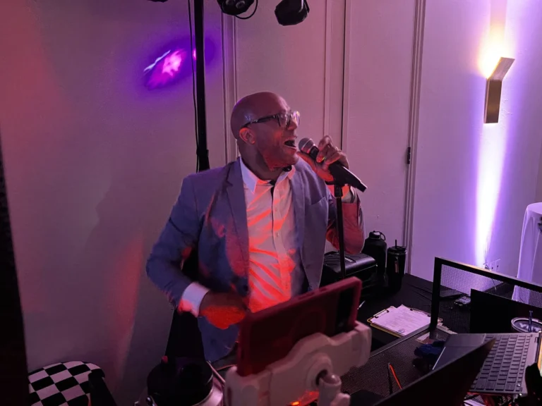 Emcee leaning into the microphone to hype the crowd beside the DJ booth on a black and white checkered floor