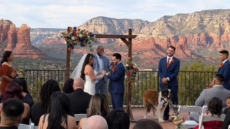 Wedding ceremony under a floral arch with the Sedona red rocks behind and guests seated in rows